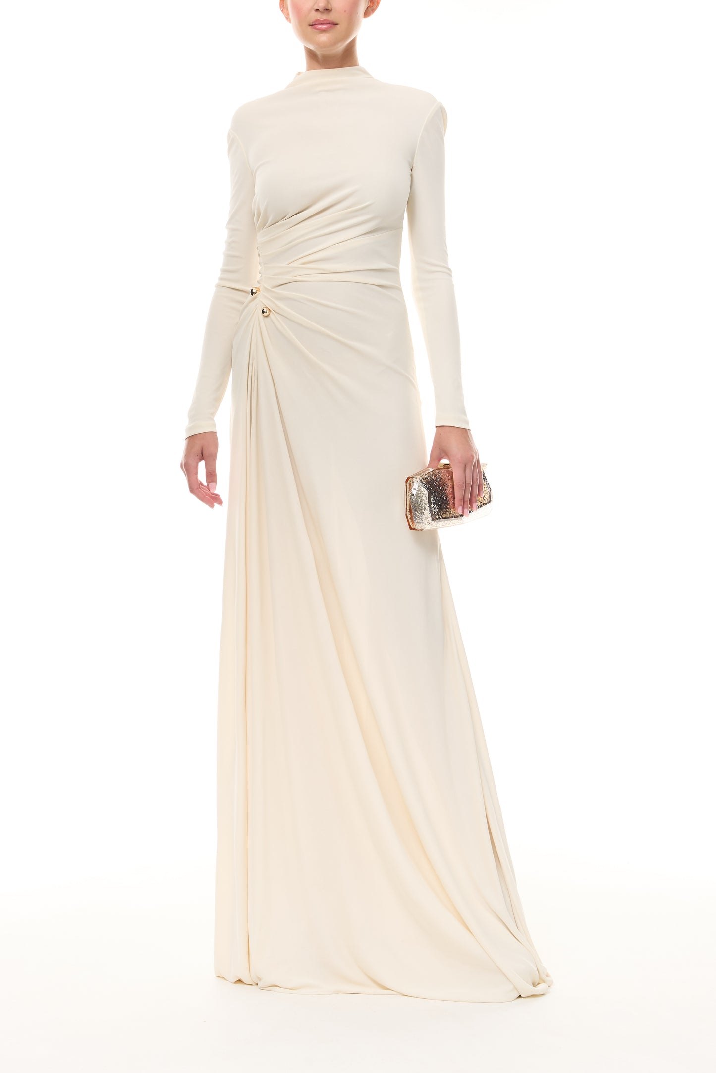Monique Lhuillier Spring 2026 Ivory crepe jersey high neck long sleeved draped gown with slit and gold ball piercing - front with Champagne Viv Minaudiere. 