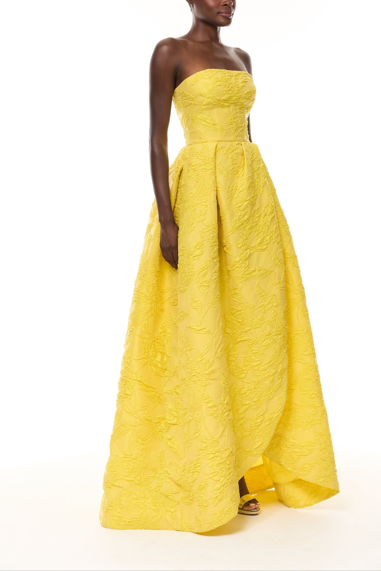 Monique Lhuillier Spring 2026- wearing Buttercup Botanical Matelassé strapless draped gown with slit - side.