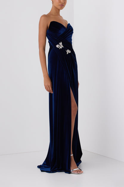 Monique Lhuillier Fall 2026 Navy stretch velour draped gown with slit and silver floral embellishment - side.