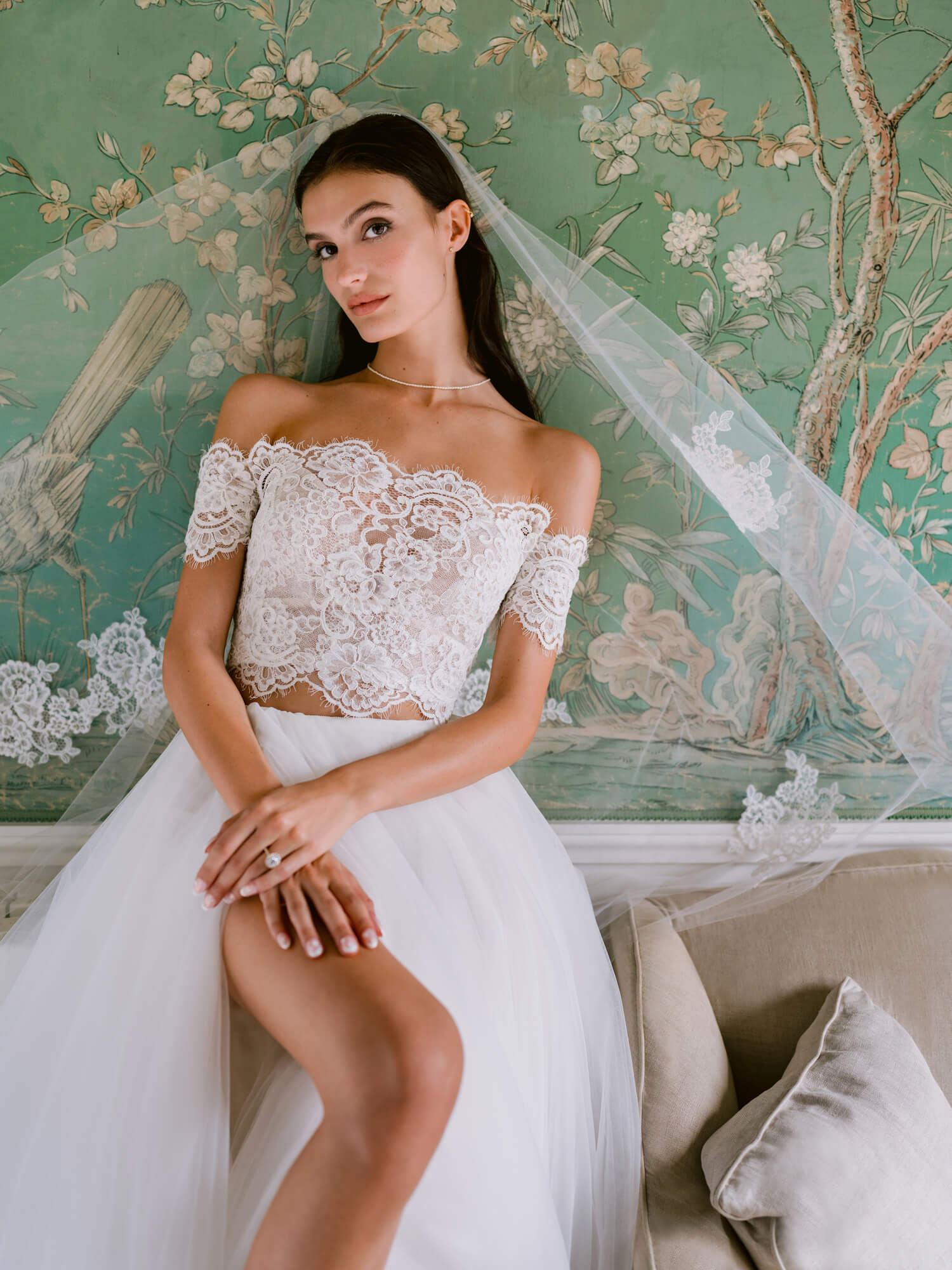 Woman wearing Monique Lhuillier Fall 2024 white lace off-the-shoulder Mimi top with tulle a-line skirt with slit