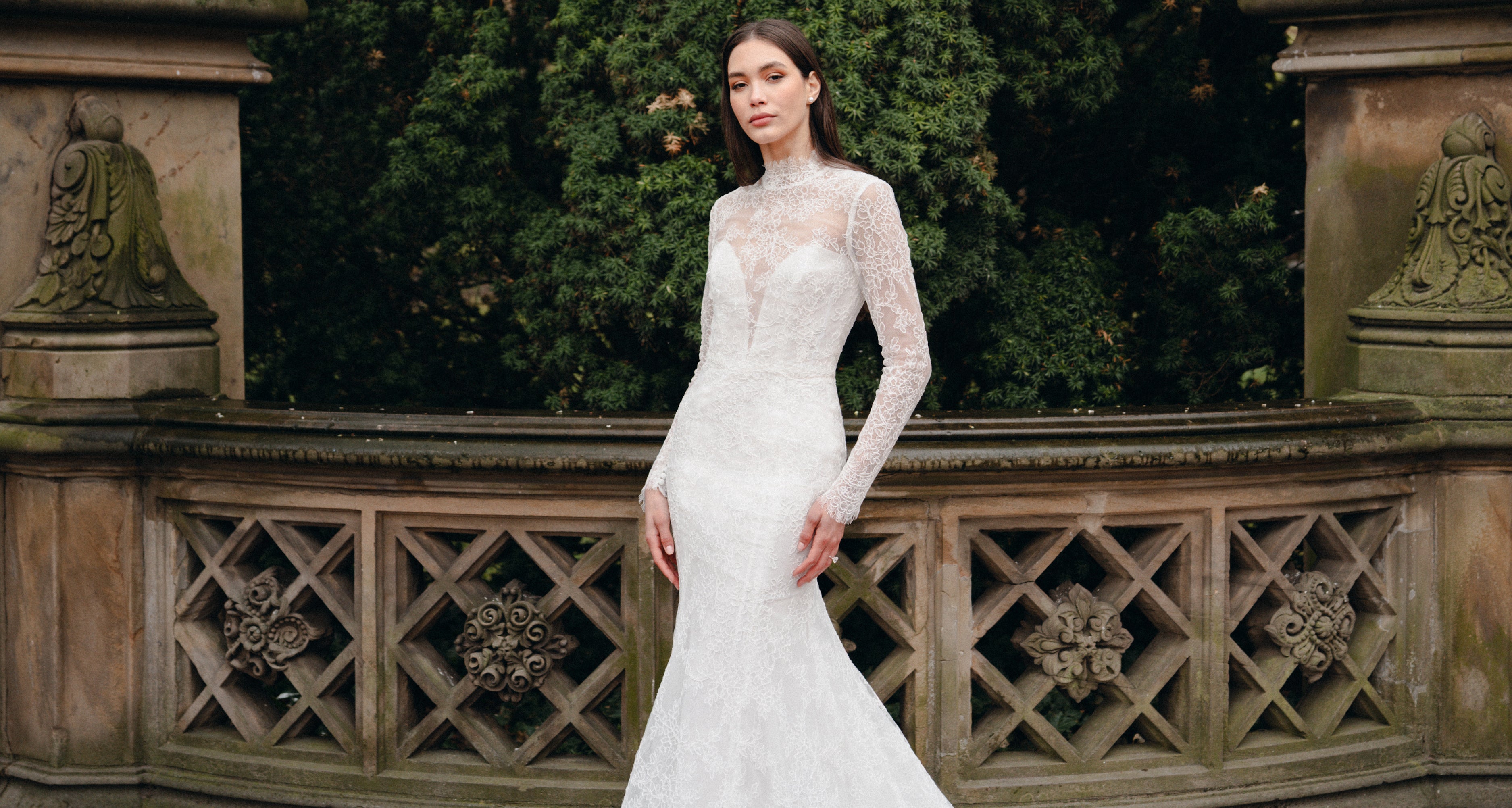 Woman wearing long sleeve high neck lace trumpet gown outside.
