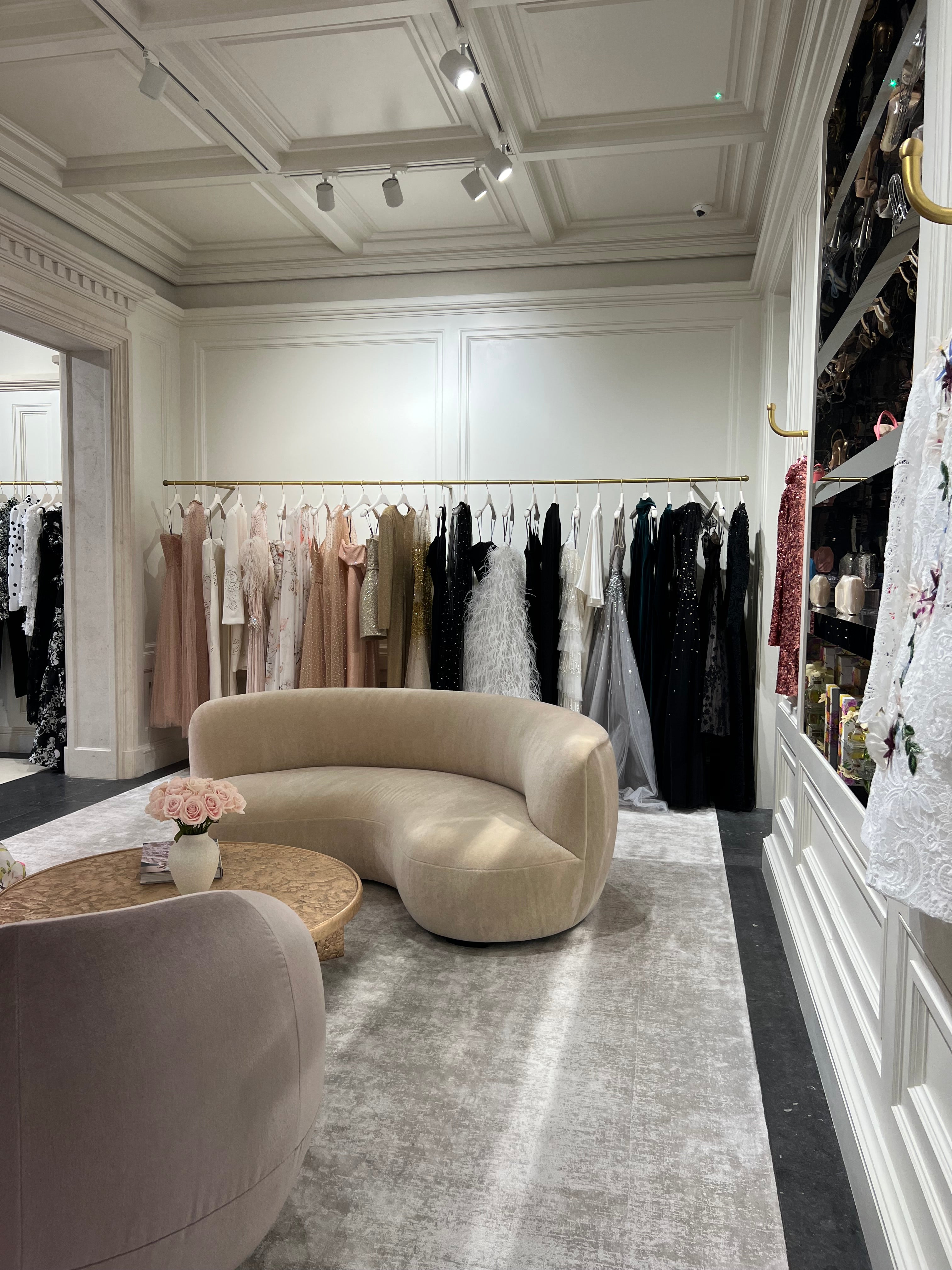 Interior of London flagship store featuring Ready to Wear, beige velvet couches, a grey carpet and pink roses on a gold table. 