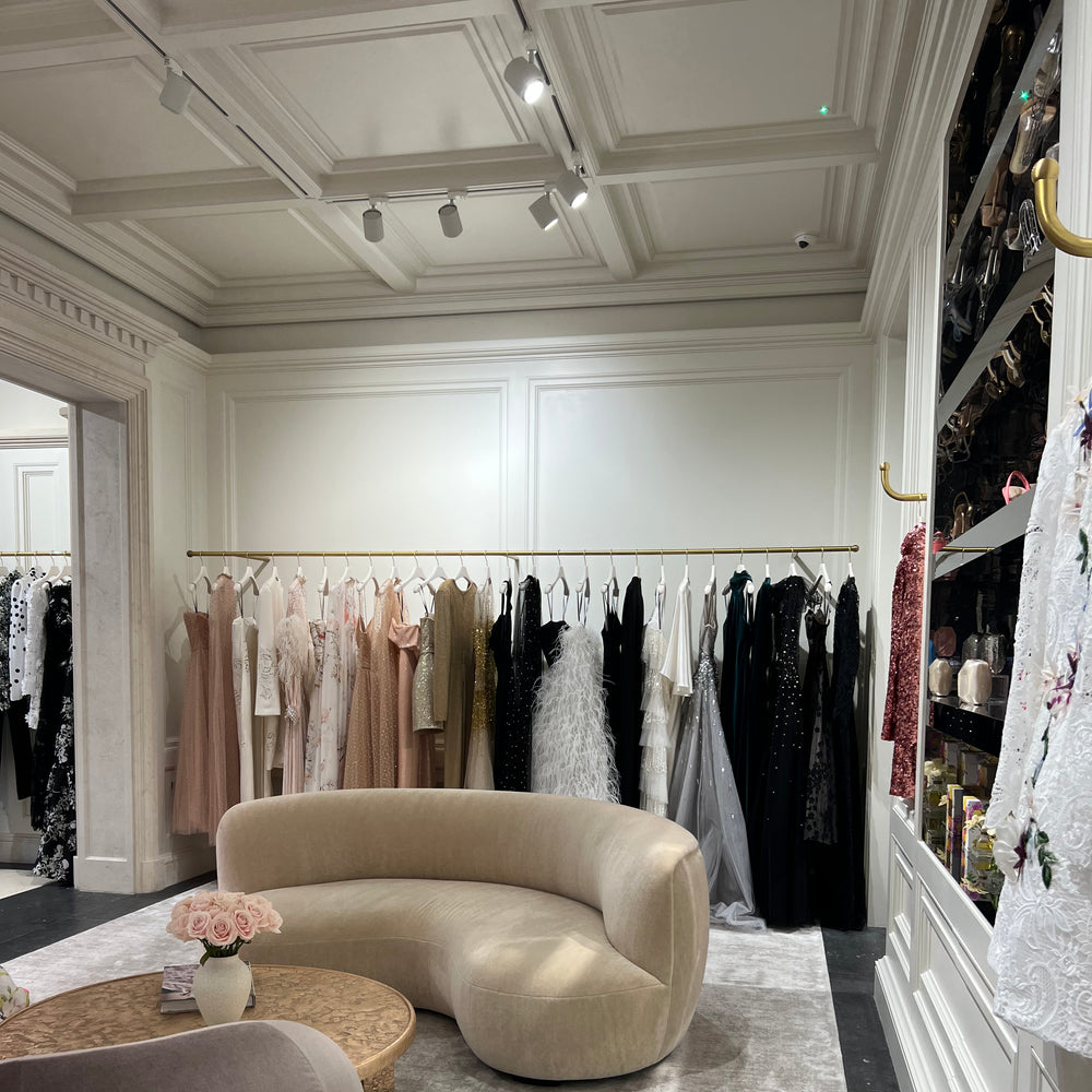 Interior of London flagship store featuring Ready to Wear, beige velvet couches, a grey carpet and pink roses on a gold table.