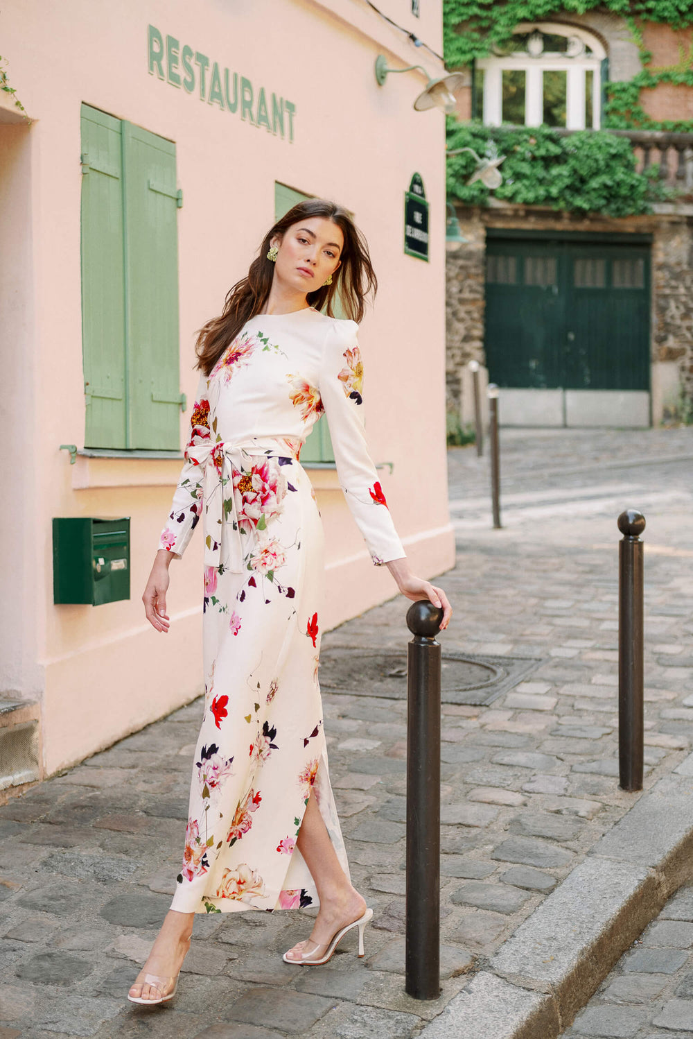 Monique Lhuillier Spring 2024 jewel neck, tea-length gown with long sleeves and self-tie sash in silk white floral fabric.