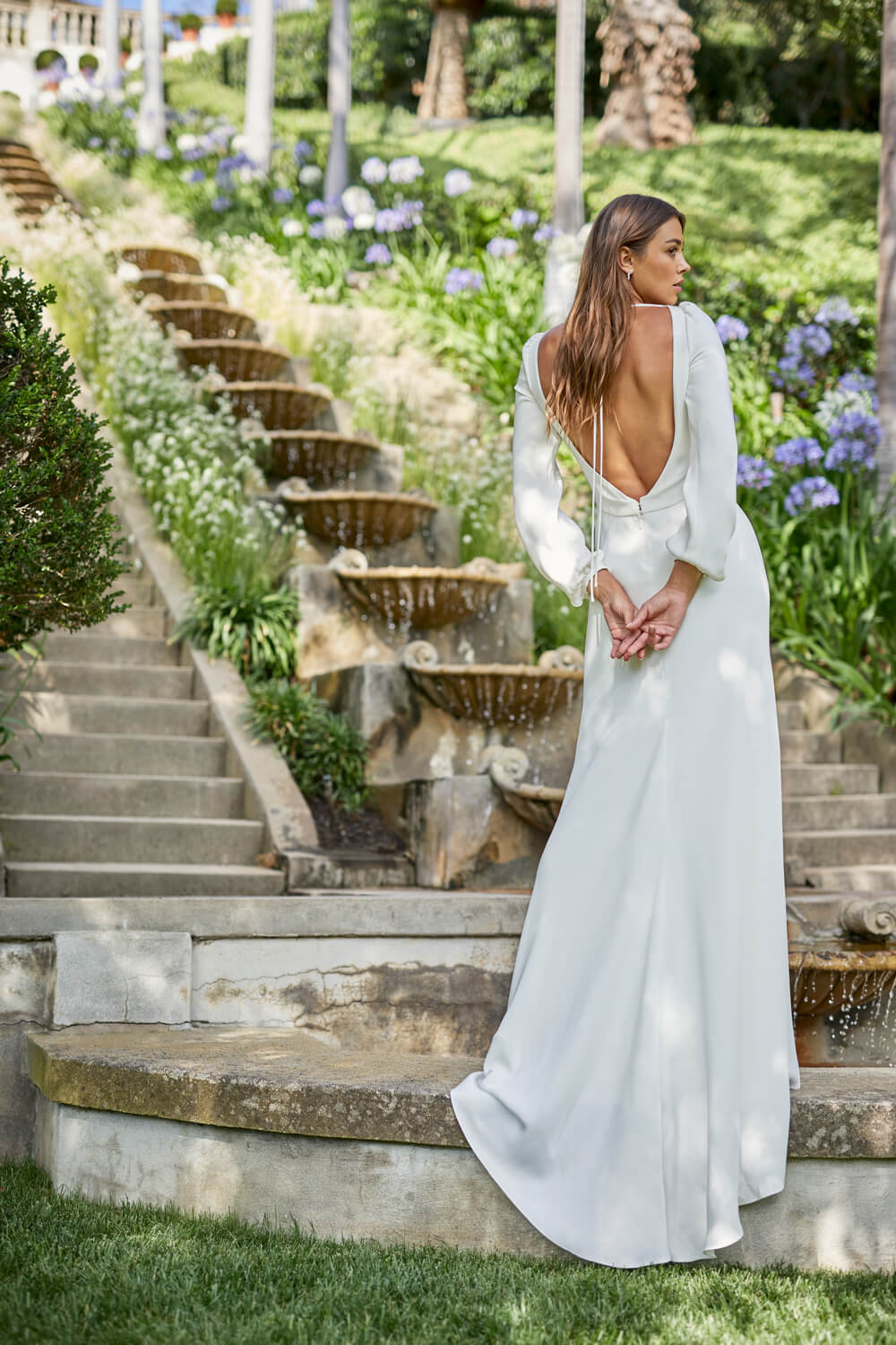 Woman wearing white, long sleeve, sheath silk crepe Monique Lhuillier Spring 2021 Roxy gown with open back