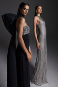 Monique Lhuillier Fall 2026: model on left wearing Noir embroidered crepe strapless deco sheath gown; model on right wearing silver embroidered tulle halter column gown- lookbook.