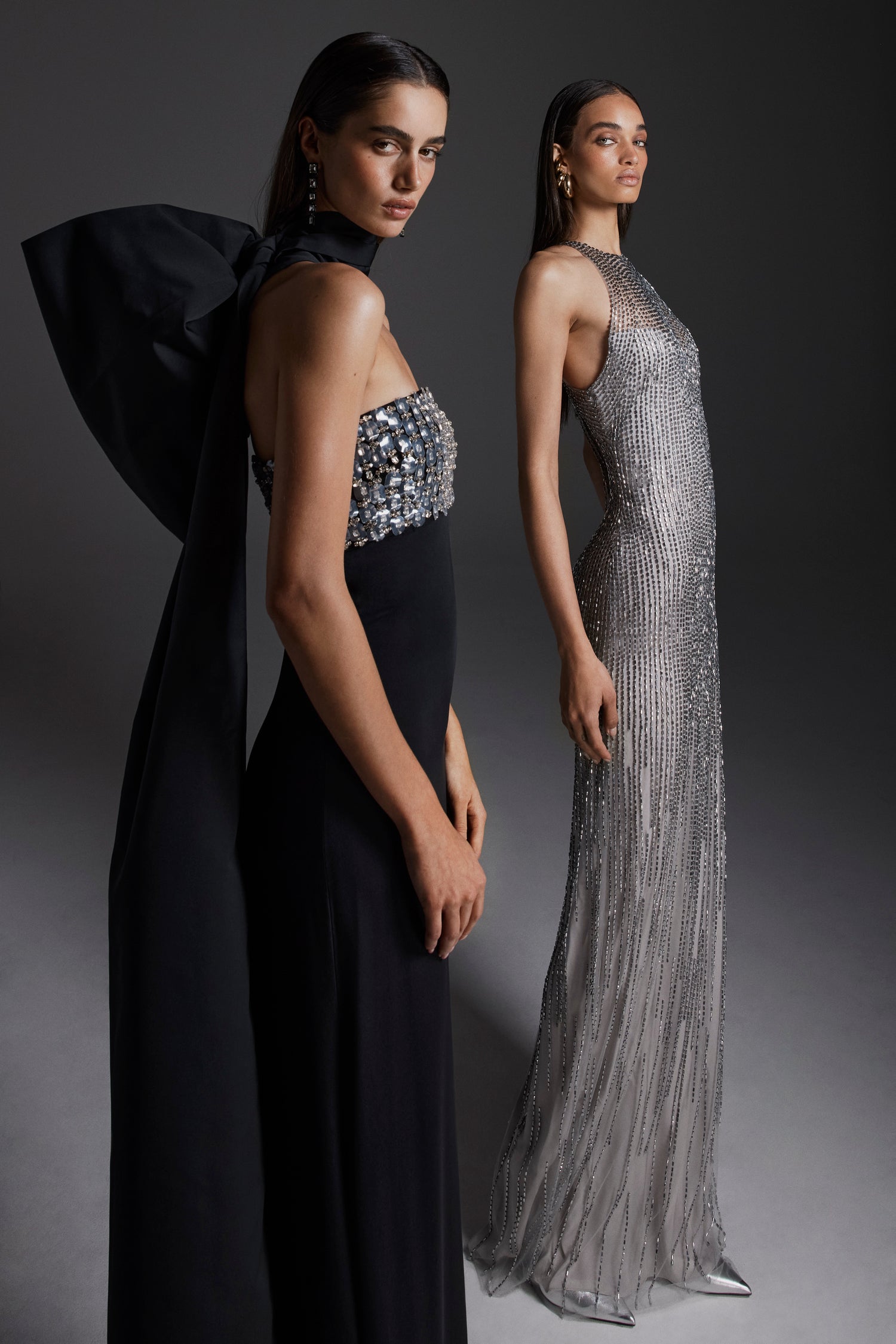 Monique Lhuillier Fall 2026: model on left wearing Noir embroidered crepe strapless deco sheath gown; model on right wearing silver embroidered tulle halter column gown- lookbook.