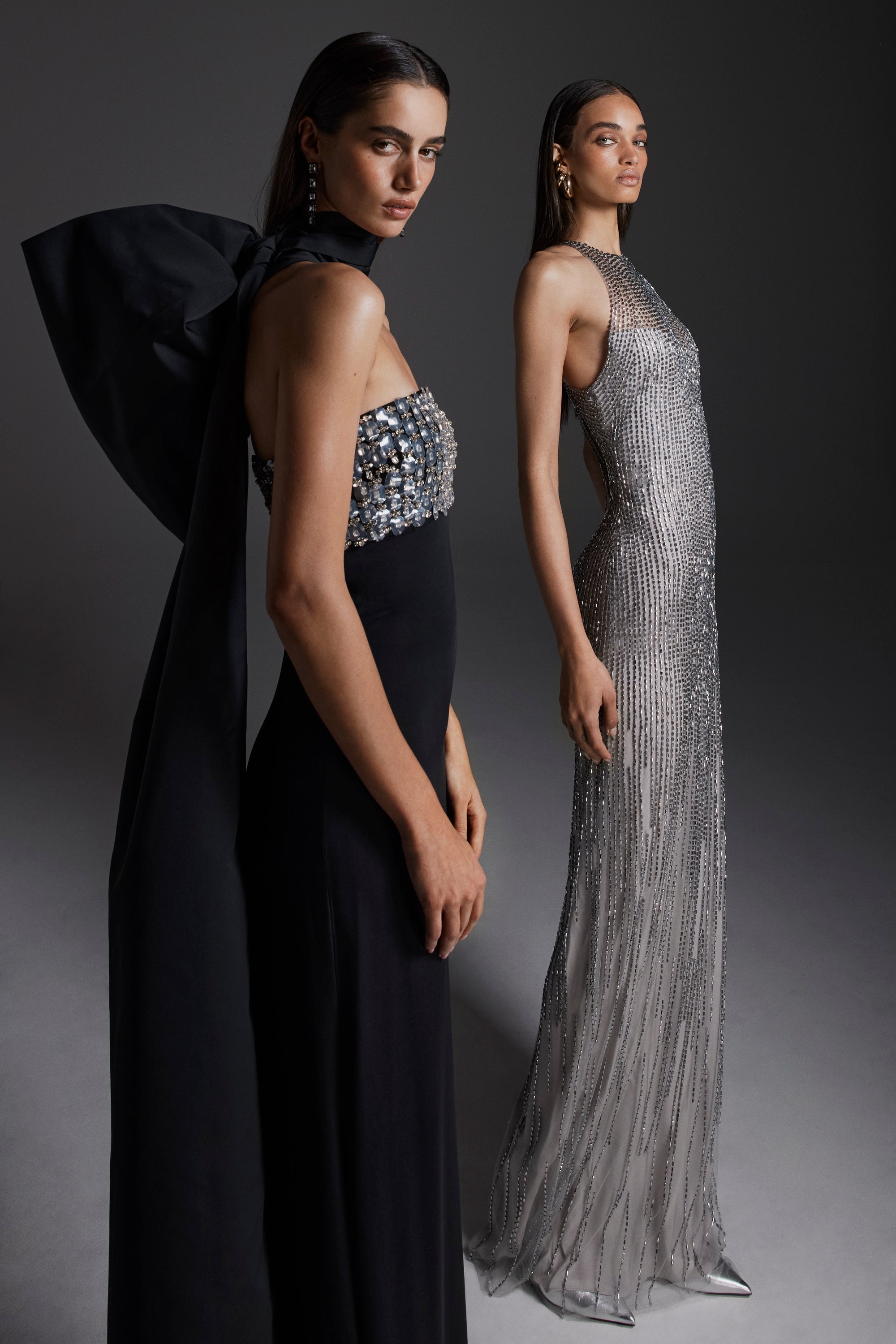 Monique Lhuillier Fall 2026: model on left wearing Noir embroidered crepe strapless deco sheath gown; model on right wearing silver embroidered tulle halter column gown- lookbook.