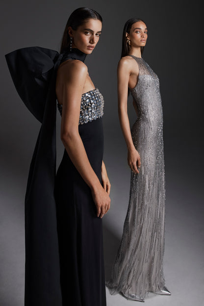 Monique Lhuillier Fall 2026: model on left wearing Noir embroidered crepe strapless deco sheath gown; model on right wearing silver embroidered tulle halter column gown- lookbook.