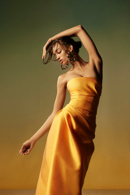 Monique Lhuillier Spring 2026 lookbook image - model wearing Mikado Mango strapless corseted draped gown with slit 