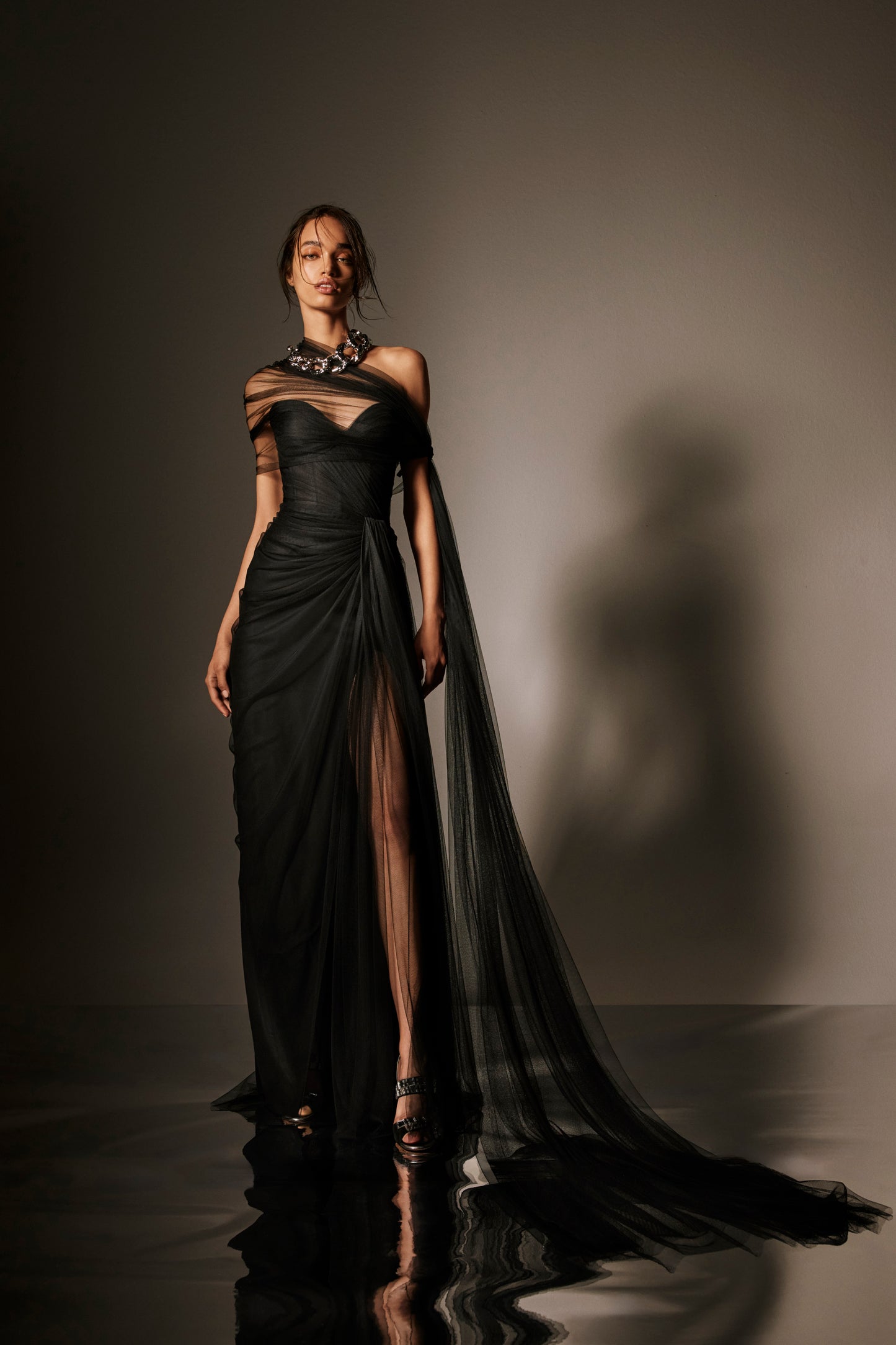 Monique Lhuillier Spring 2026 lookbook image - model wearing noir spanish tulle draped strapless gown with detachable wrap and streamers