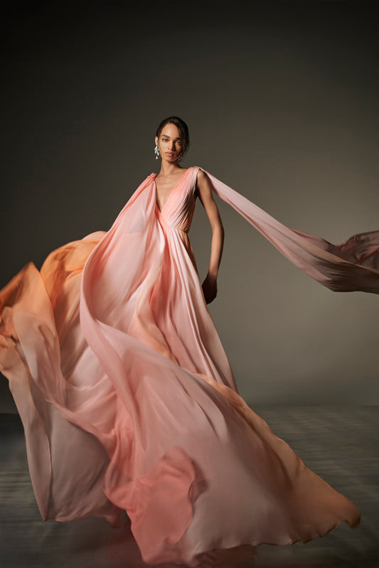 Monique Lhuillier Spring 2026 lookbook image - model wearing Plumeria ombre chiffon pleated v-neck gown with streamers