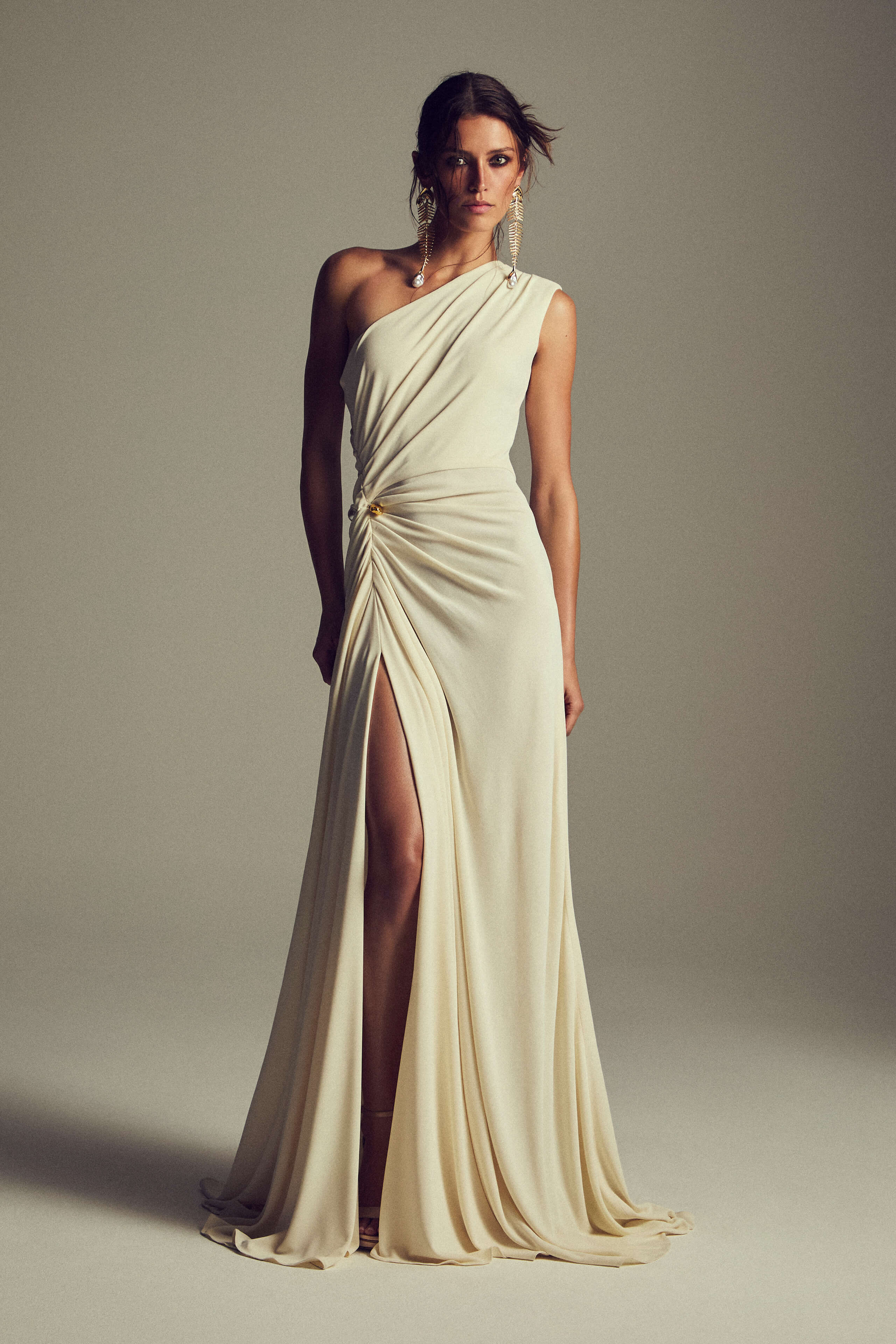 Monique Lhuillier Spring 2027 Ivory Crepe Jersey one-shoulder draped gown with slit and gold piercing at hip - lookbook.