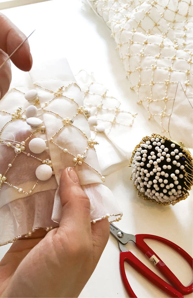 Monique Lhuillier atelier behind the scenes - close up of ivory and gold embroidered gown with pin cushion, needle and scissors. 