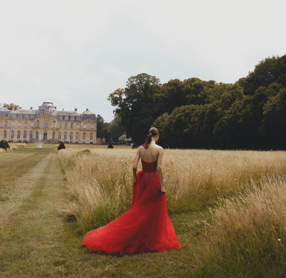 Monique Lhuillier strapless ballgown in cherry red embroidered tulle - model walking through grass.