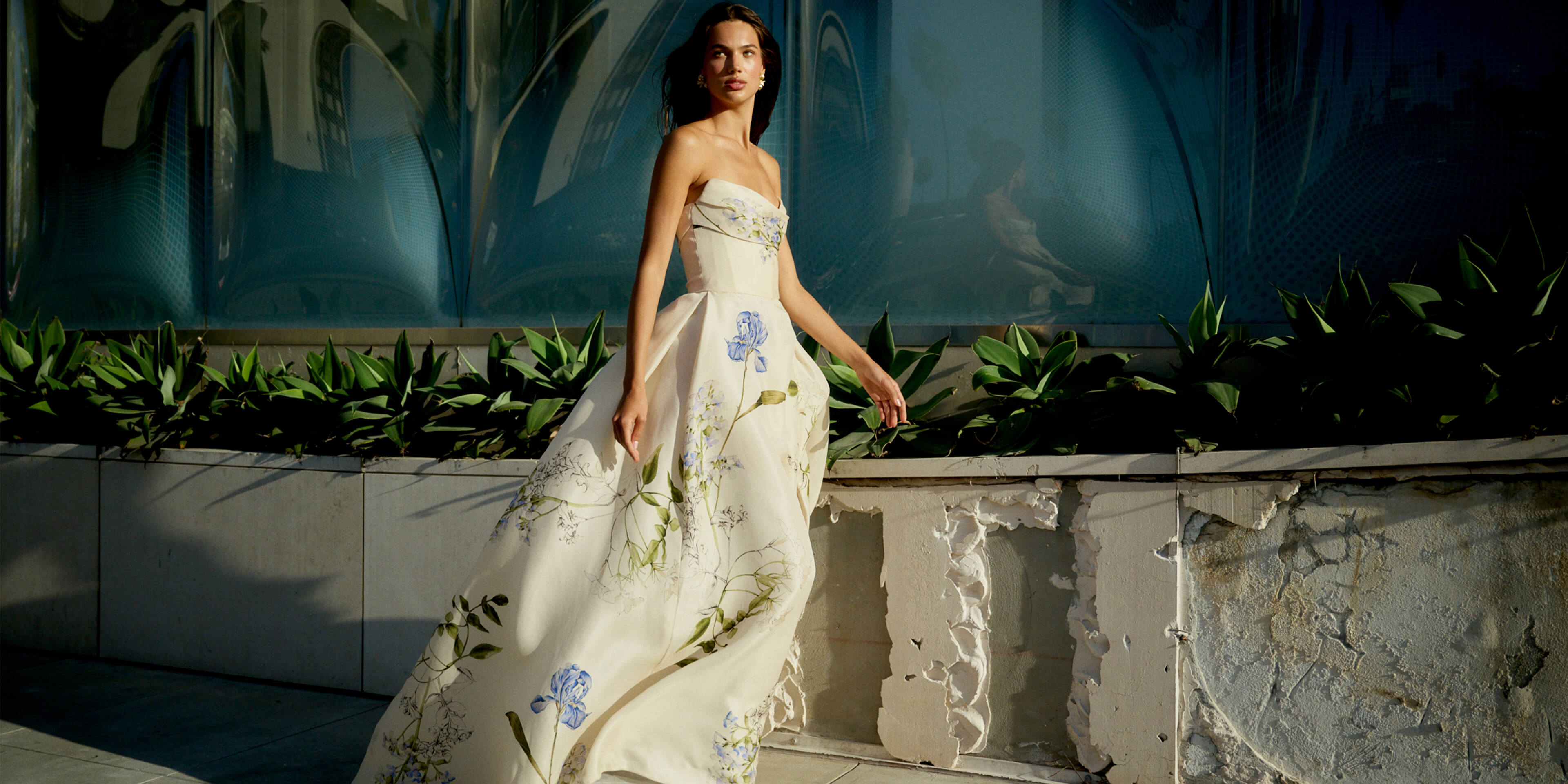 Monique Lhuillier Spring 2026 Ivory Multi Iris Bouquet Printed Gazar Draped bodice
ball gown with front skirt slit - model on sidewalk outside.