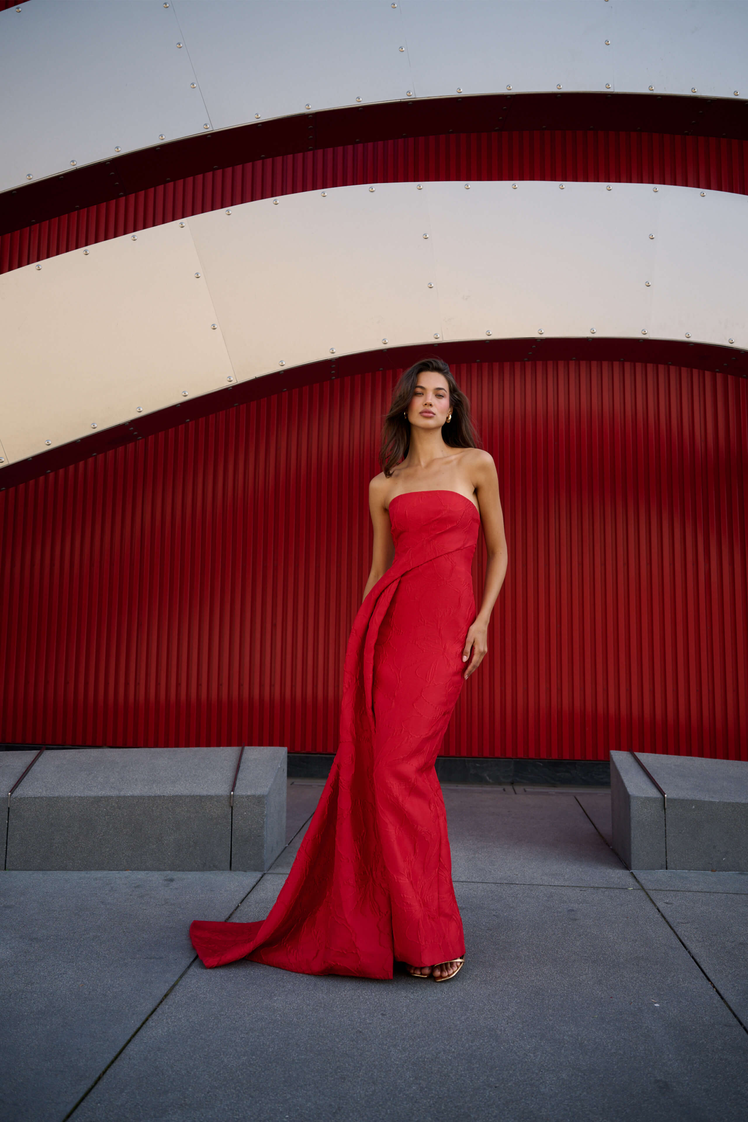 Monique Lhuillier Spring 2026 Poppy Linear Rose Jacquard Strapless Strapless draped column gown with train - model standing on sidewalk.