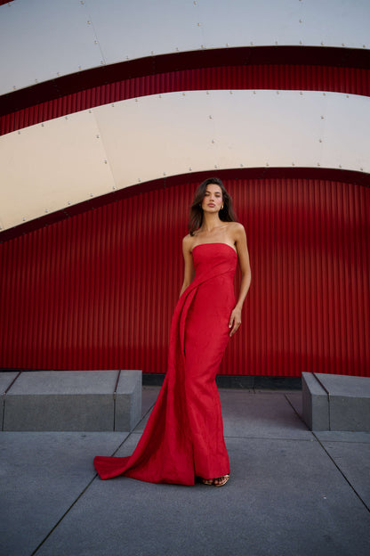 Monique Lhuillier Spring 2026 Poppy Linear Rose Jacquard Strapless Strapless draped column gown with train - model standing on sidewalk.