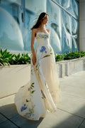 Monique Lhuillier Spring 2026 Ivory Multi Iris Bouquet Printed Gazar Draped bodice
ball gown with front skirt slit - model on sidewalk outside.