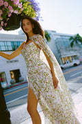 Monique Lhuillier Fall 2026 Silk White/Multi Ivy Bloom Printed Silk Chiffon Strapless asymmetric draped bodice gown with front slit - model on sidewalk outside.