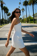 Monique Lhuillier Spring 2026 White Cotton Tweed strapless sculpted mini dress - model walking on crosswalk outside.