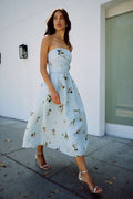 Monique Lhuillier Fall 2026 Breeze/Multi Floating Posies Printed Gazar strapless tea-length dress - model walking outside on sidewalk.