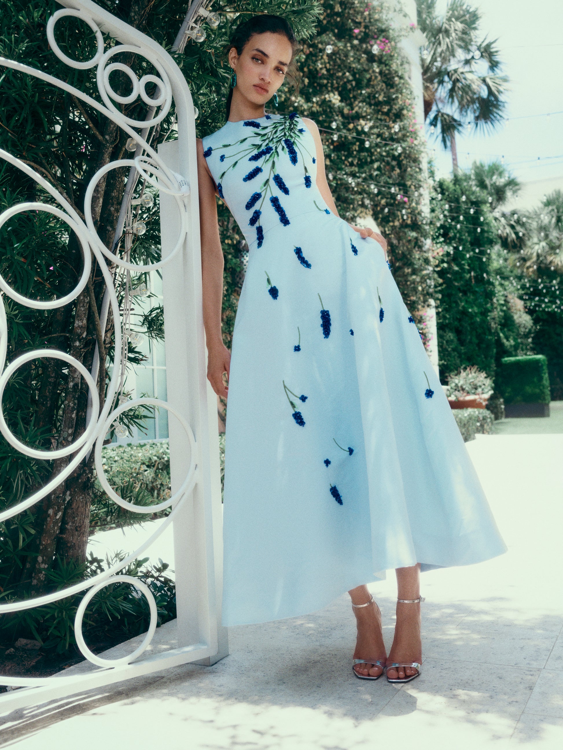 Monique Lhuillier Spring 2025 Sleeveless, tea-length dress with pockets in Powder Blue faille with Lavender-patterned embroidery - lookbook photo on model.