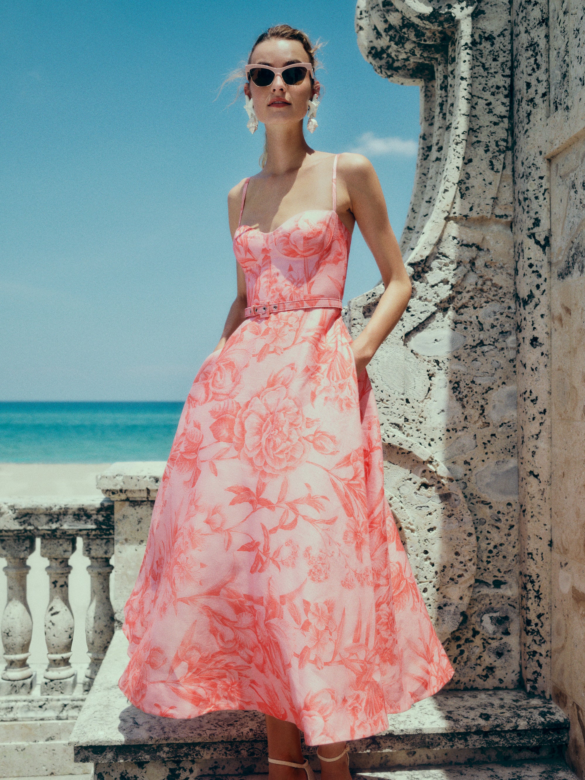 Monique Lhuillier Spring 2025 Floral printed a-line midi dress with spaghetti straps, corseted bodice and pockets in Rosette Coral colored linen - lookbook photo.