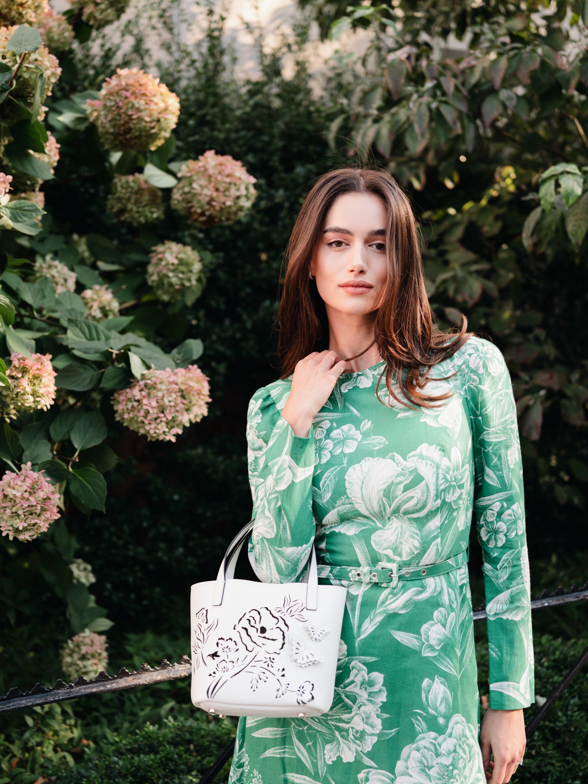 Leather top handle mini tote bag with laser cut florals, three-dimensional leather butterflies and small zip pouch in Ivory- on model in green floral print dress.