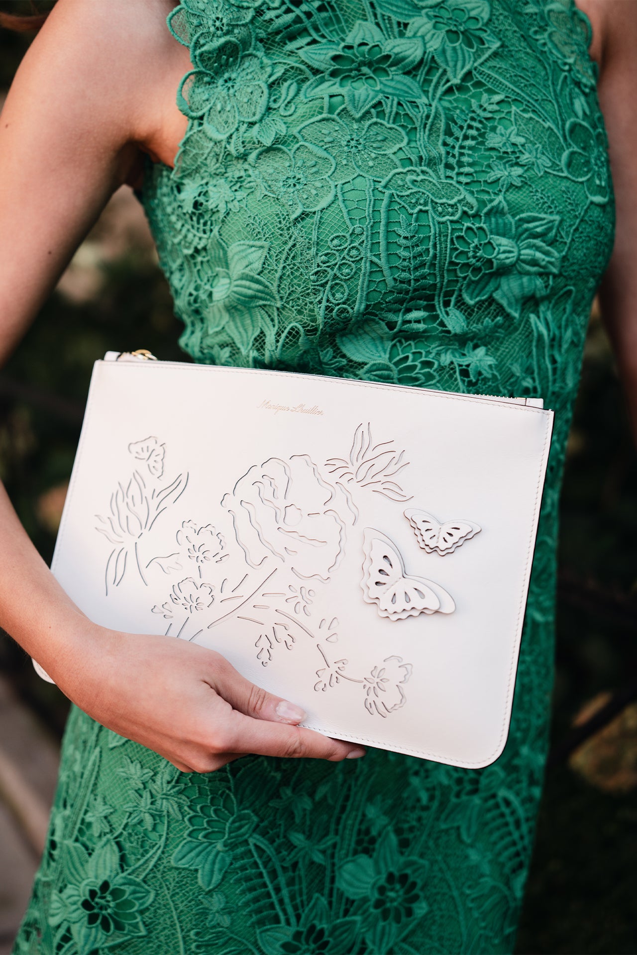 Leather zip pouch with laser cut florals and three-dimensional leather butterflies in Ivory- on model wearing green lace dress.