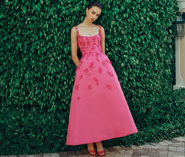 Monique Lhuillier Spring 2025 pink floral embroidered spaghetti strap tea-length
a-line dress on model in front of wall of greenery