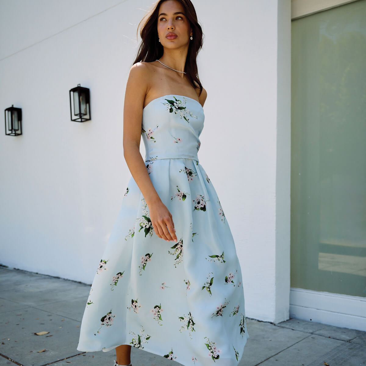 Monique Lhuillier Fall 2026 Breeze/Multi Floating Posies Printed Gazar strapless tea-length dress - model walking outside on sidewalk. 