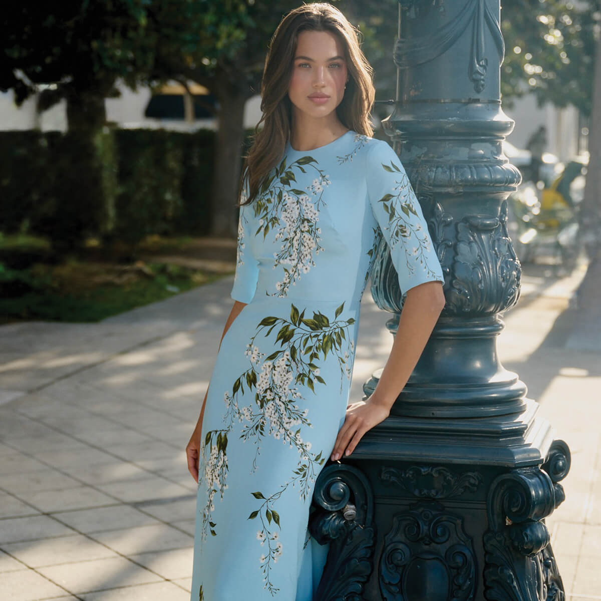 Monique Lhuillier Fall 2026 Horizon Blue Multi Wisteria Printed Crepe Short sleeve gown - model on sidewalk outside leaning on lamp post.