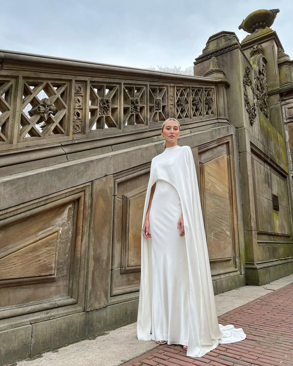 Monique Lhuillier Bridal Spring 2023 draped crepe satin Viola gown with spaghetti straps and low back, paired with matching round neck Viola cape.