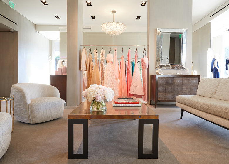 Image of Los Angeles flagship store with evening gowns, a crystal chandelier, a coffee table and chairs