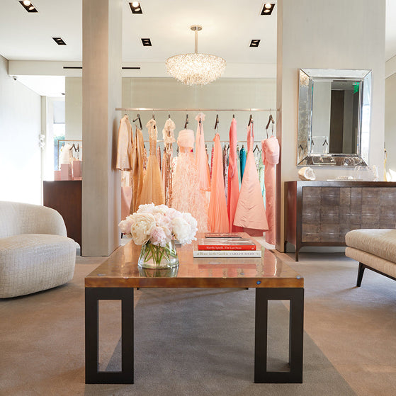 Image of Los Angeles flagship store with evening gowns, a crystal chandelier, a coffee table and chairs