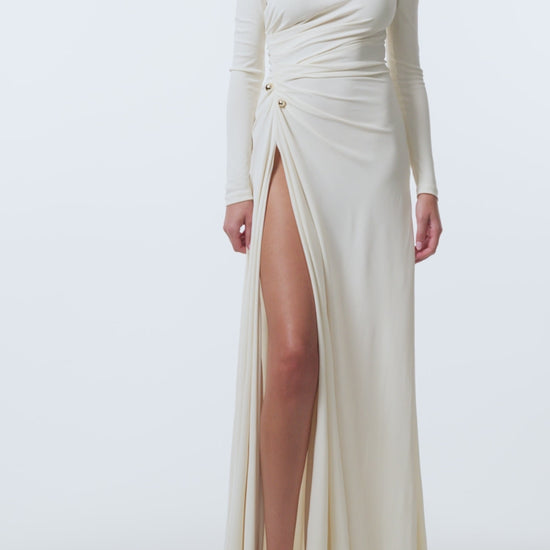 Monique Lhuillier Spring 2026 Ivory crepe jersey high neck long sleeved draped gown with slit and gold ball piercing - video.