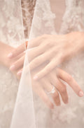 Folded hands in front of lace gown with engagement ring under layer of tulle