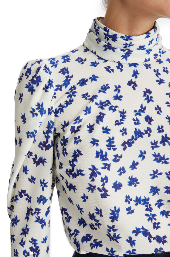 Close up of woman in silk white and blue floral crepe blouse with high neck and long sleeves.